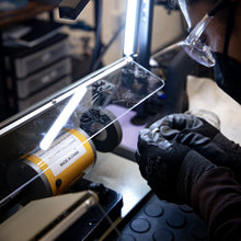 Load image into Gallery viewer, A person in safety gear uses a bench lathe to polish a metal ring during a jewelry making workshop at Halie & Co.
