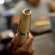 Load image into Gallery viewer, A person secures a silver ring with a green stone in a wooden clamp during a silversmithing workshop.
