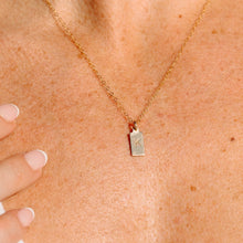 Load image into Gallery viewer, A close-up of a person’s chest wearing the Alphabet Initial Rectangle Necklace—a gold filled necklace featuring a rectangular pendant engraved with the letter K. A hand with manicured nails rests gently on their shoulder.