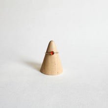 Load image into Gallery viewer, The Carnelian Thin Band Ring | Size 4, featuring a slender band with a small round orange Carnelian stone, is displayed on a cone-shaped wooden ring holder against a plain white background.