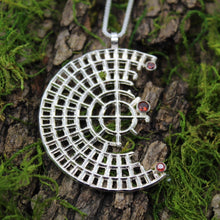 Load image into Gallery viewer, The Sterling Silver Perfect Imperfection Garnet and Fire Citrine Necklace, featuring a geometric crescent pendant adorned with three fiery red gemstones, rests on textured tree bark with patches of green moss.