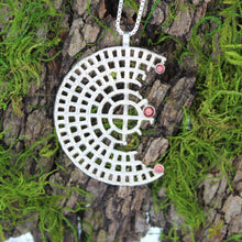 Load image into Gallery viewer, The Sterling Silver Perfect Imperfection Garnet and Fire Citrine Necklace features a geometric, circular grid design accented with three small garnet gems, hanging elegantly on a chain against a mossy tree bark background, making this necklace both striking and refined.