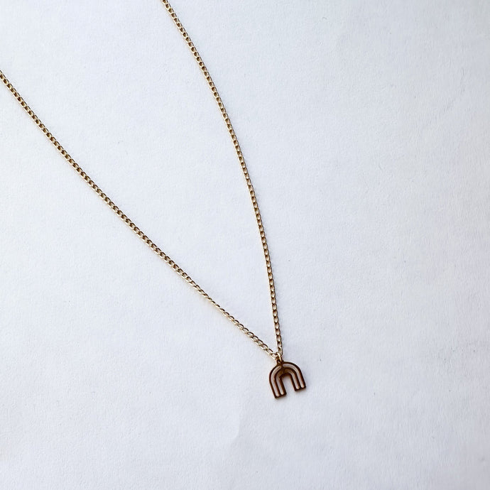Gold necklace with a rainbow shaped pendant on a white background